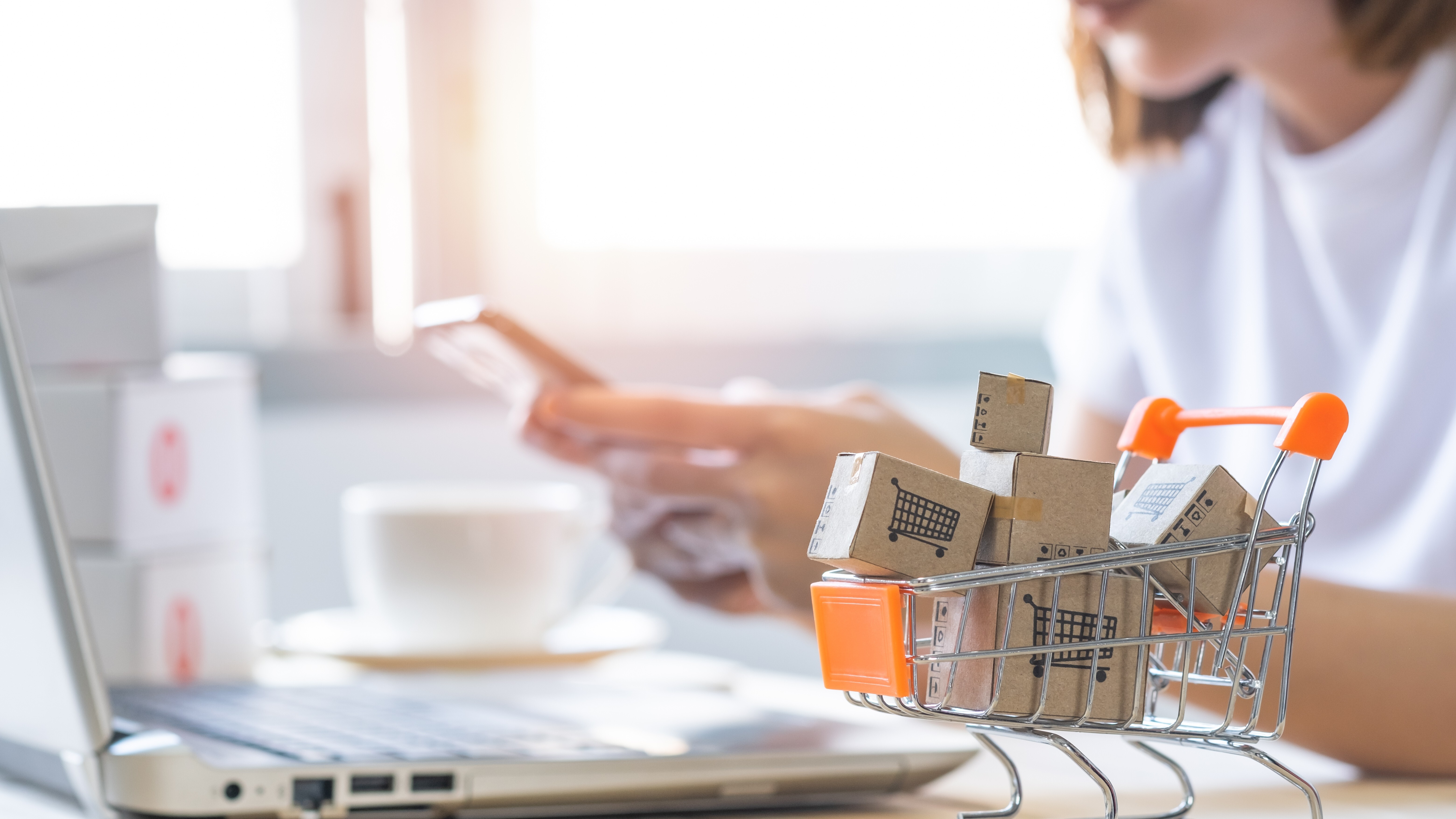 Shopping cart with Paper box or parcel with blur background woman holding mobile phone. Businesswoman or entrepreneur working from home. Online shopping, e-commerce,internet banking, spending money.